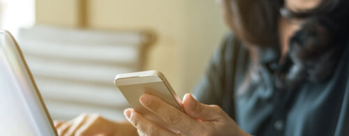 Mulher segurando o celular e olhando para a tela do computador