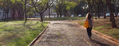 Estudante vista de costas caminhando na Praça da Paz da Unicamp carregando mochila amarela no ombro