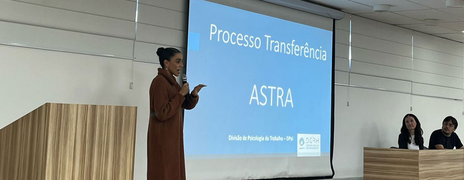 Coordenadora DPsi no palco com slide sobre o ASTRA ao fundo