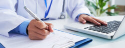 Mãos de médica escrevendo no formulário e digitando no teclado