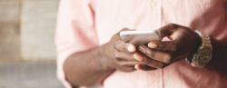 Foco nas mãos de homem negro digitando no celular com fundo desfocado