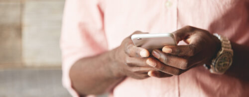 Foco nas mãos de homem negro digitando no celular com fundo desfocado