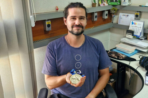 Brunno segurando uma medalha no seu local de trabalho