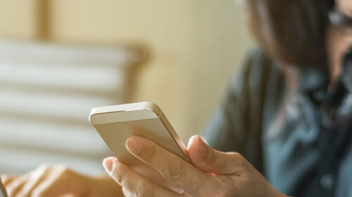 Mulher segurando o celular com uma mão e digitando em botebook com a outra