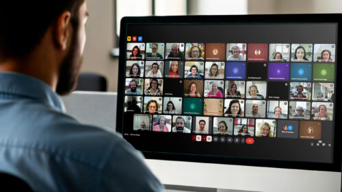 Homem olhando para tela do computador onde está acontecendo uma reunião online com muitos participantes